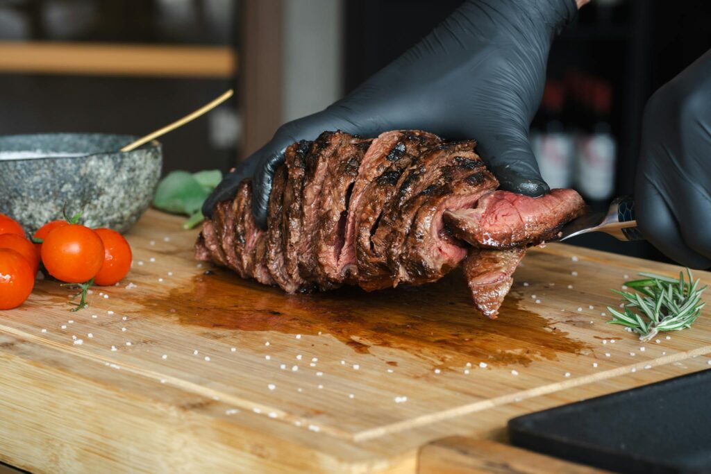 Chef slicing tender, juicy steak with precision on a wooden cutting board, accompanied by fresh herbs.