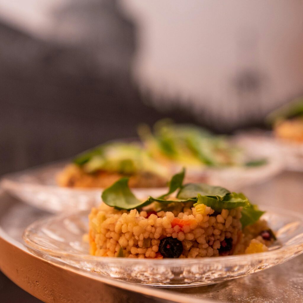 Close-up of a gourmet couscous dish, artfully plated with fresh vegetables on a clear glass plate.