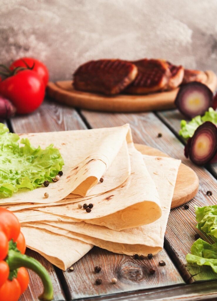 Close-up of fresh tortilla wraps surrounded by grilled vegetables, perfect for a healthy meal.